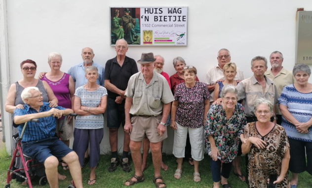 Resident of Huis Wag 'n Bietjie in front of plaque